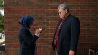 Two people facing each other. One speaking and the other is a reporter taking notes.